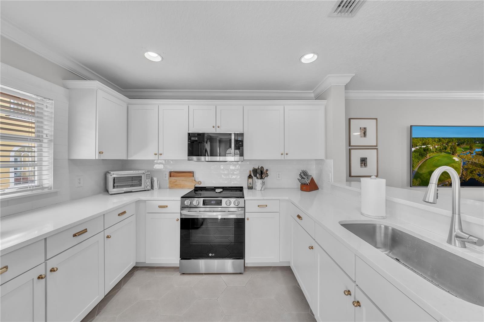 Fully updated kitchen with designer Quartz, Stainless Steel Appliances, breakfast bar seating, white wooden cabinetry, and recessed lighting