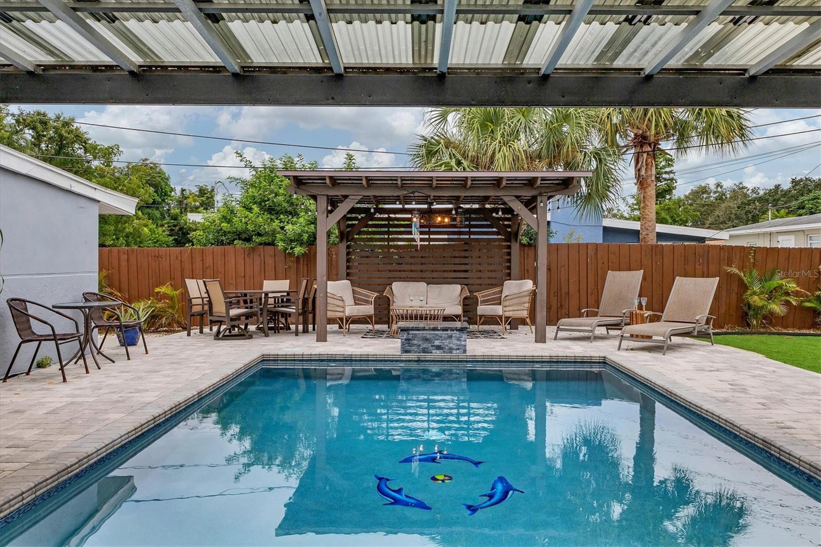Refurbished pool with tropical design, colorful tiles and a stone paver wrap around deck is partially shaded from the sun
