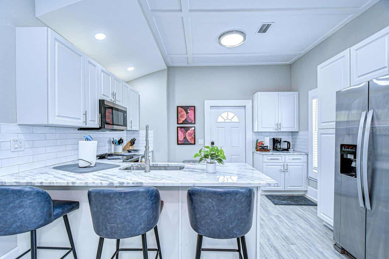 The modern kitchen features sleek white cabinetry, stainless steel appliances, and a marble-look countertop with bar seating. Perfectly designed for both cooking and entertaining, this space blends style with functionality.