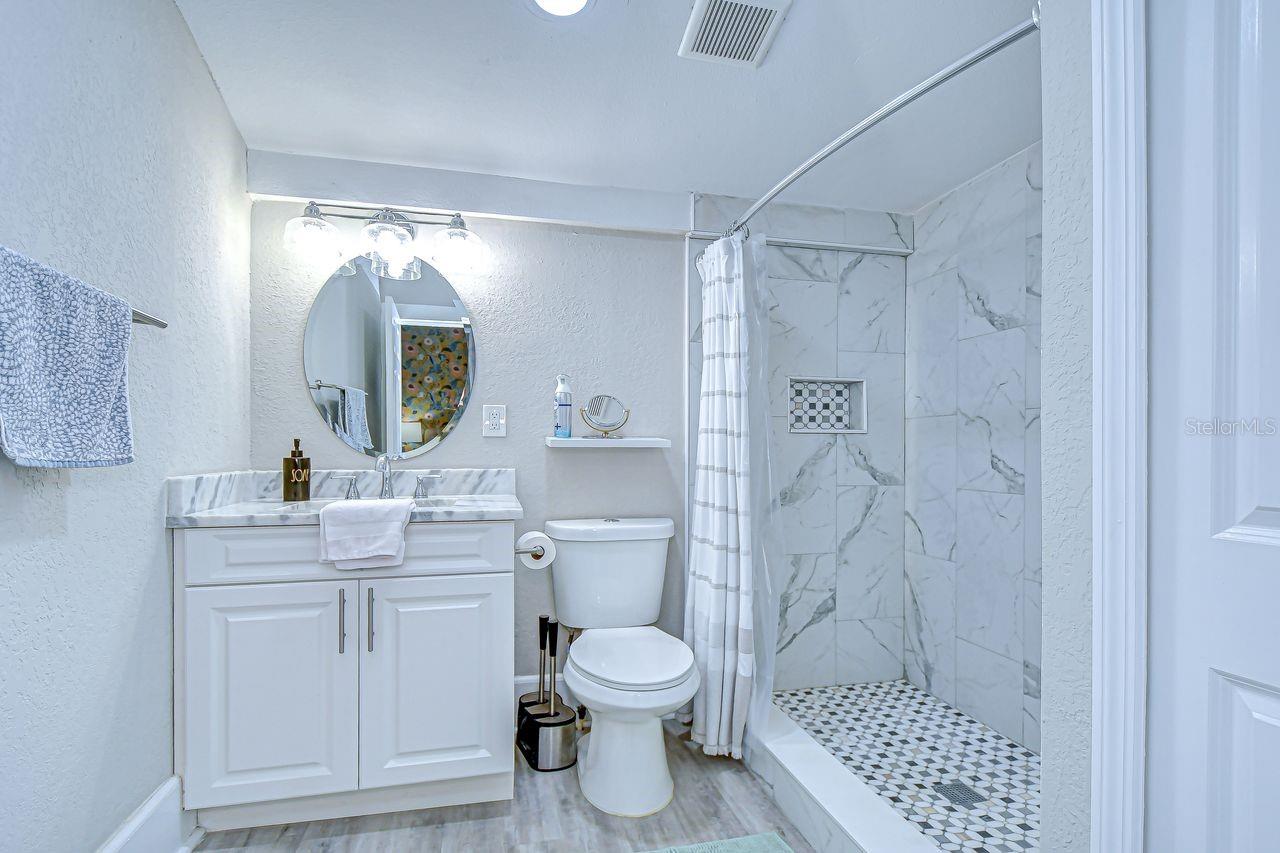 The primary bathroom boasts a marble-tiled walk-in shower, modern vanity, and sleek finishes throughout.