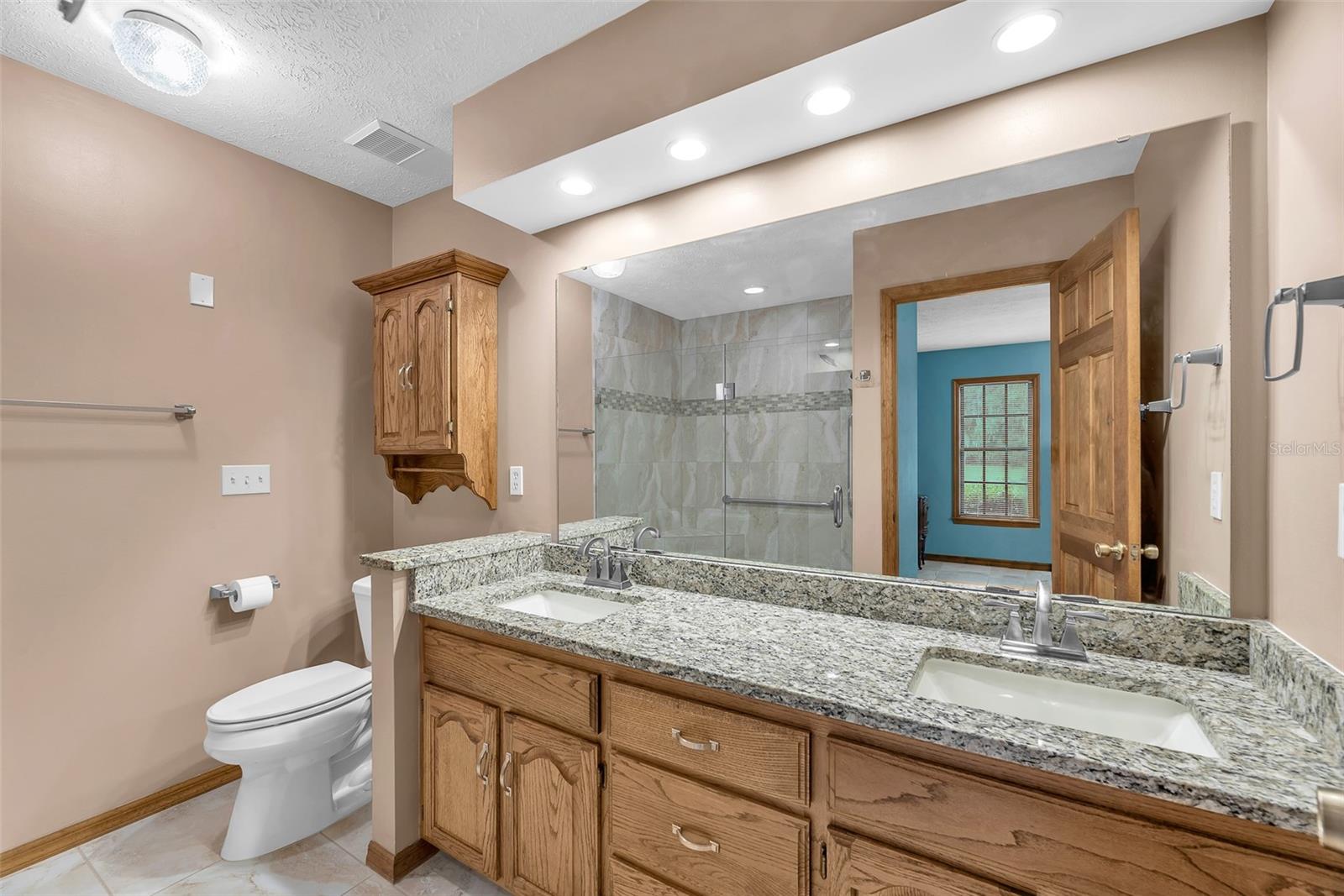 The ensuite features an oversized no-threshold shower, a large vanity with dual sinks and modern natural finishes.