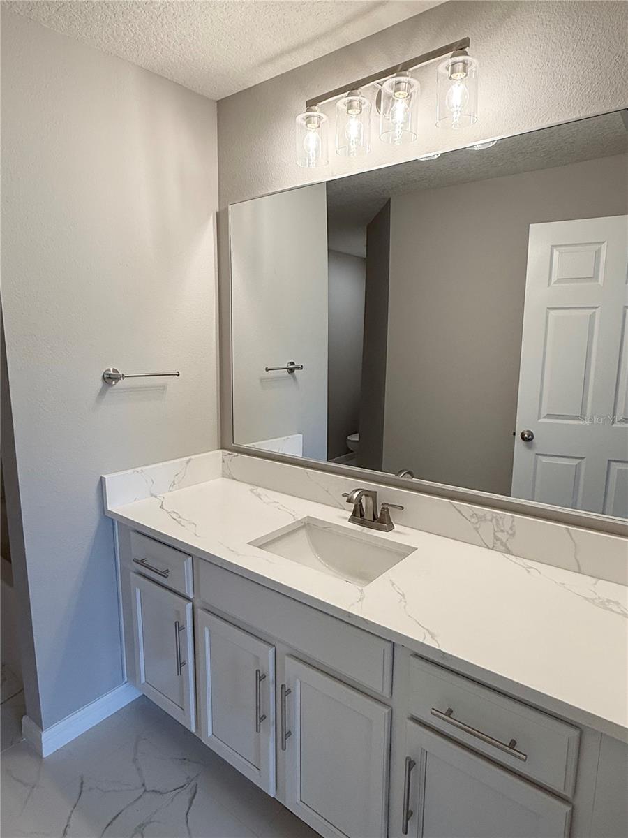 Primary bathroom exudes spa like modern feel with quartz vanity, new lighting and fixtures and newly installed marble design ceramic tile