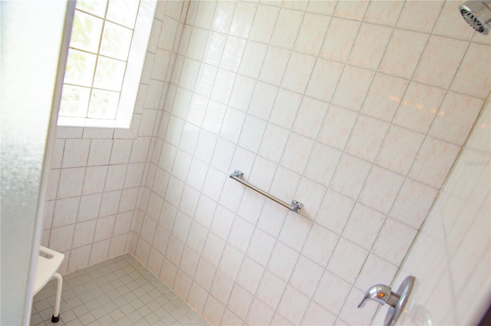 Extra-spacious walk-in shower with grab bars and window to bring in light.