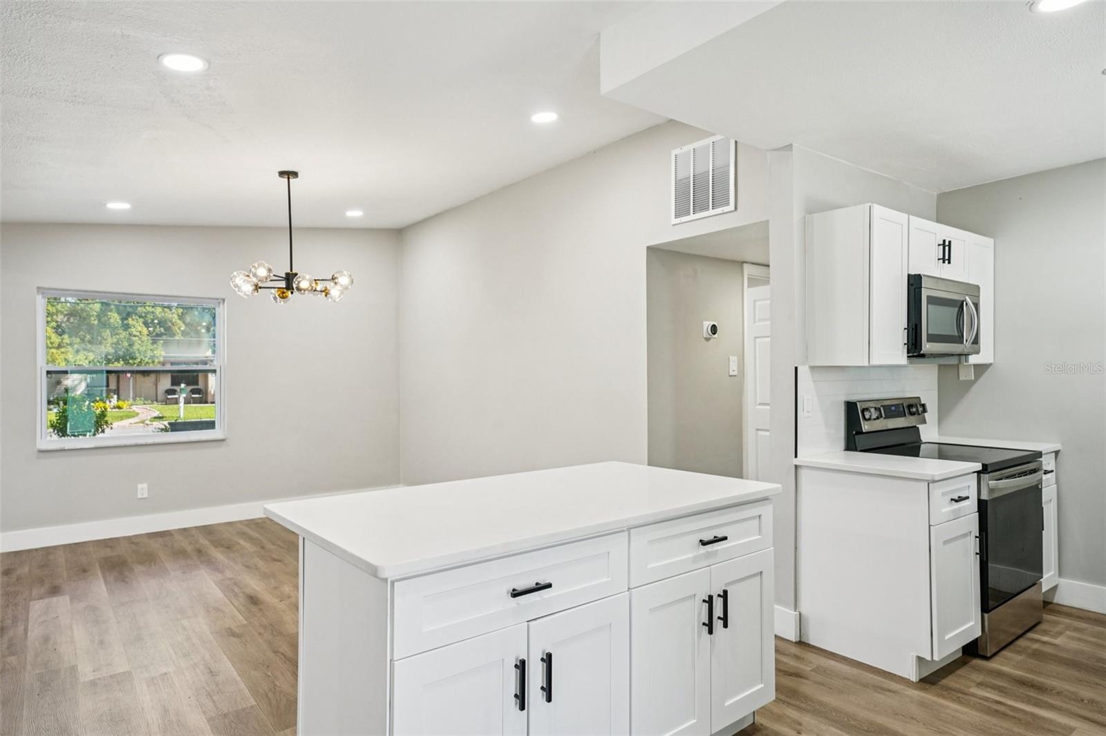 The updated kitchen is light, bright, and outfitted with timeless shaker cabinets, stainless steel appliances, a large sink, and pull-down spray faucet. A clean subway tile backsplash pairs with quartz countertops, while the central island with pull-up breakfast bar is perfect for casual dining or conversations with the cook.
