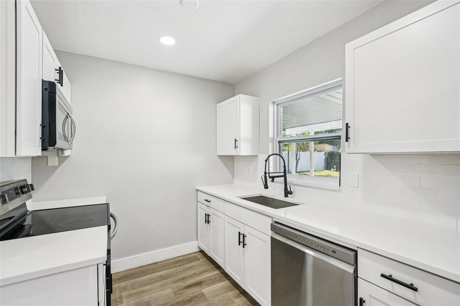 The updated kitchen is light, bright, and outfitted with timeless shaker cabinets, stainless steel appliances, a large sink, and pull-down spray faucet. A clean subway tile backsplash pairs with quartz countertops, while the central island with pull-up breakfast bar is perfect for casual dining or conversations with the cook.
