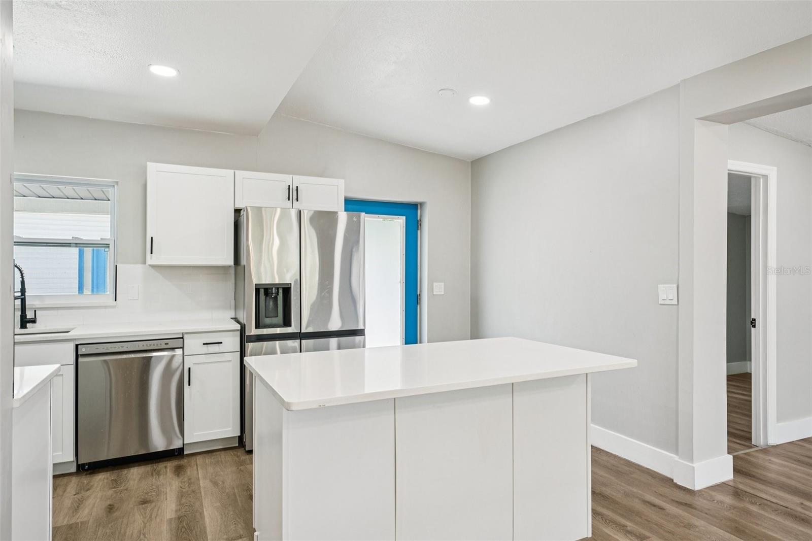 The updated kitchen is light, bright, and outfitted with timeless shaker cabinets, stainless steel appliances, a large sink, and pull-down spray faucet. A clean subway tile backsplash pairs with quartz countertops, while the central island with pull-up breakfast bar is perfect for casual dining or conversations with the cook.