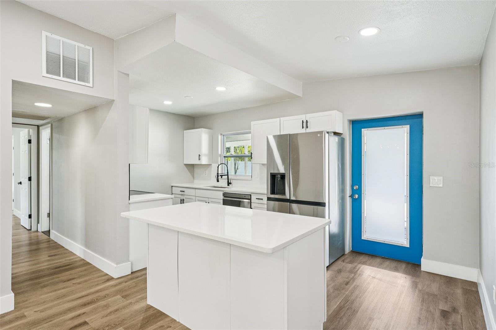 The updated kitchen is light, bright, and outfitted with timeless shaker cabinets, stainless steel appliances, a large sink, and pull-down spray faucet. A clean subway tile backsplash pairs with quartz countertops, while the central island with pull-up breakfast bar is perfect for casual dining or conversations with the cook.