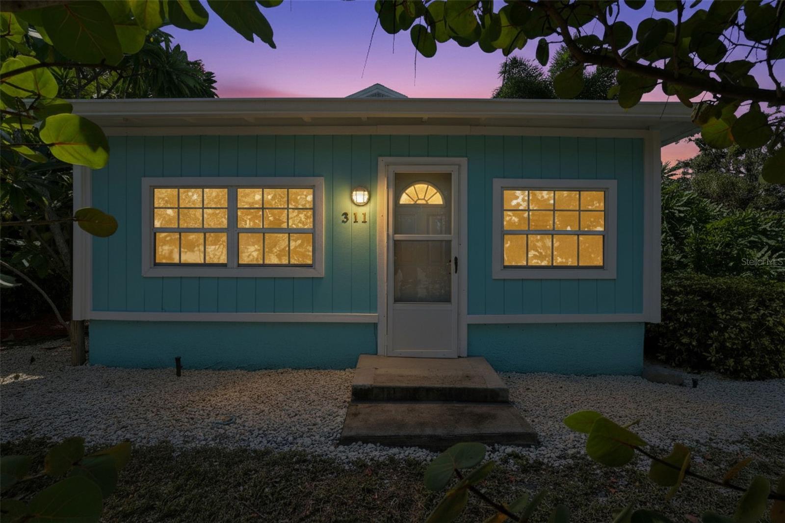 Charming Key West–style façade with fresh turquoise siding, crisp white trim, and warm window lighting that highlights the welcoming entry.