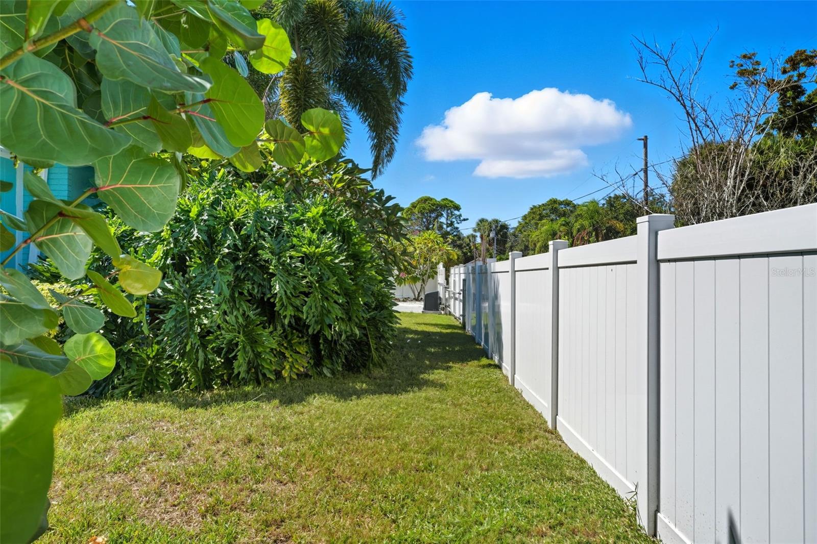 Fully fenced side yard with tropical privacy landscaping and room for gardening or pets.