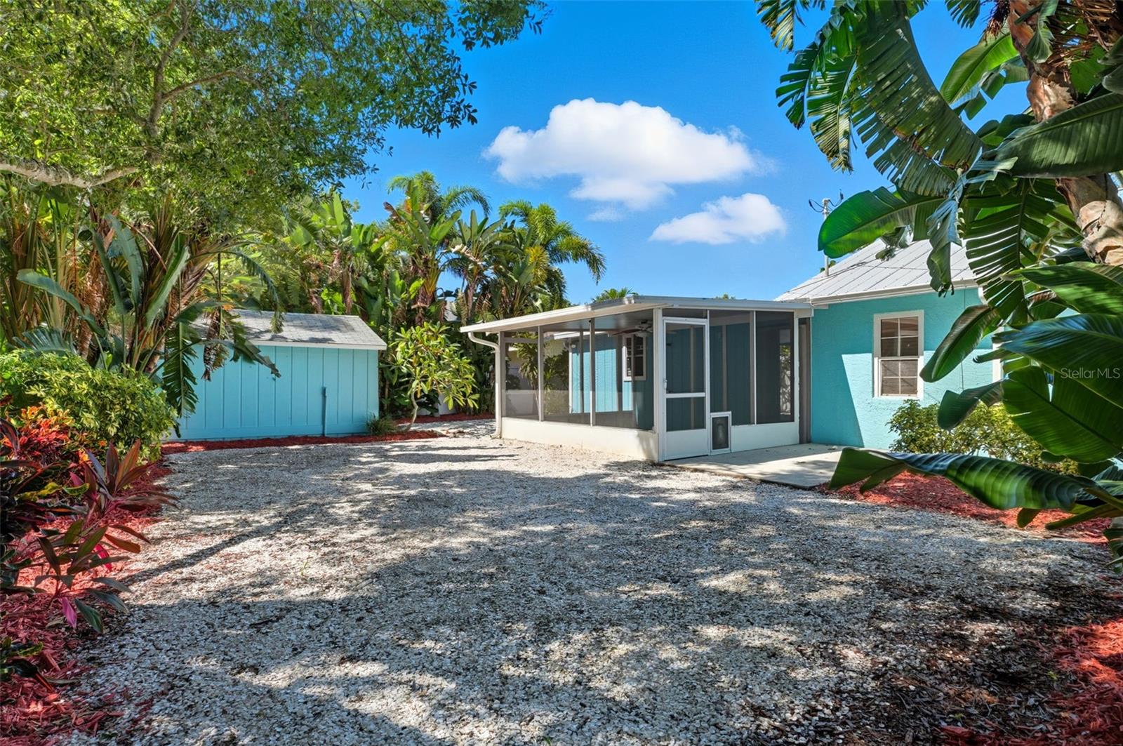 Spacious backyard featuring a screened patio and matching shed, surrounded by lush tropical foliage.