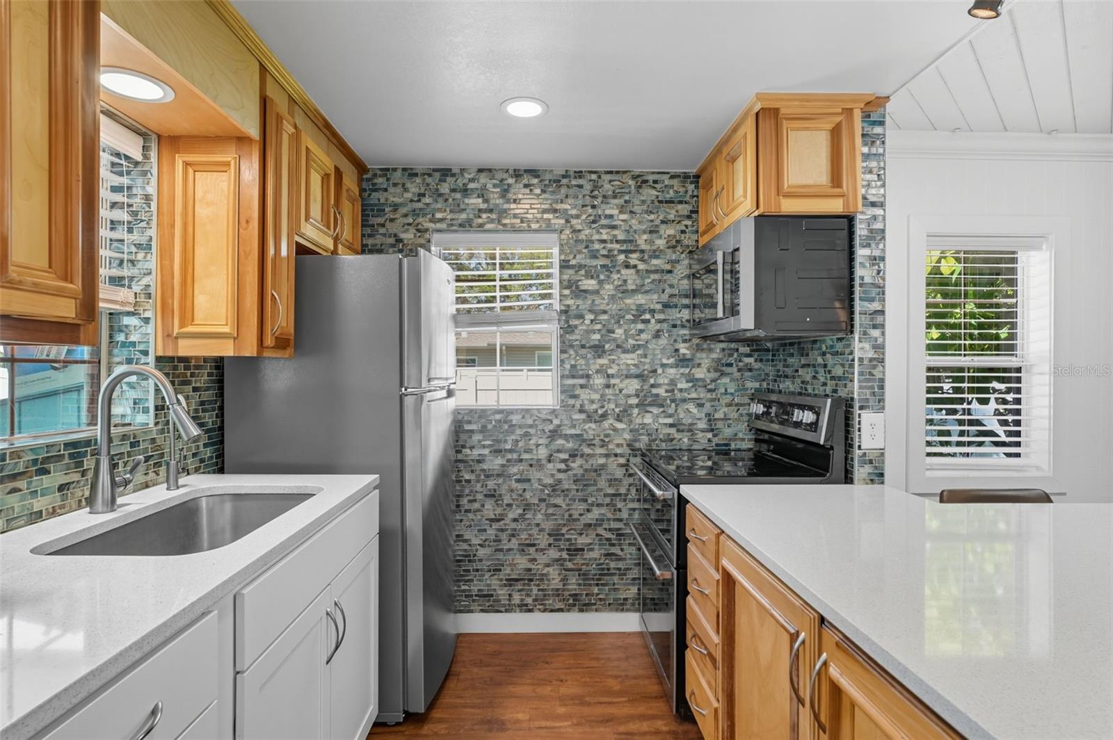 Stylish glass mosaic backsplash, stainless steel sink, and sleek appliances make this space both functional and modern.