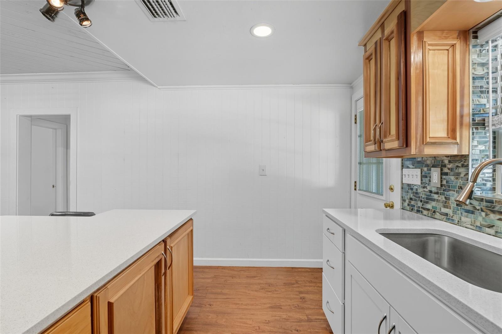 Additional prep and storage space with light cabinetry, quartz counters, and a tile backsplash for a clean coastal look.