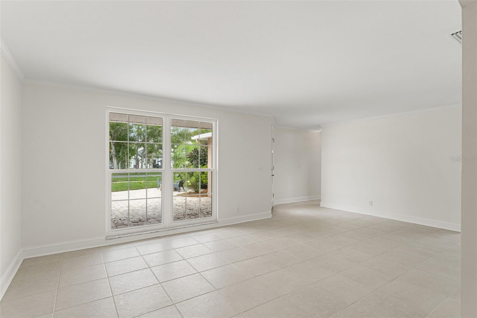 Step inside to an airy living area with neutral tile flooring, crown molding, and large picture windows filling the space with natural light.