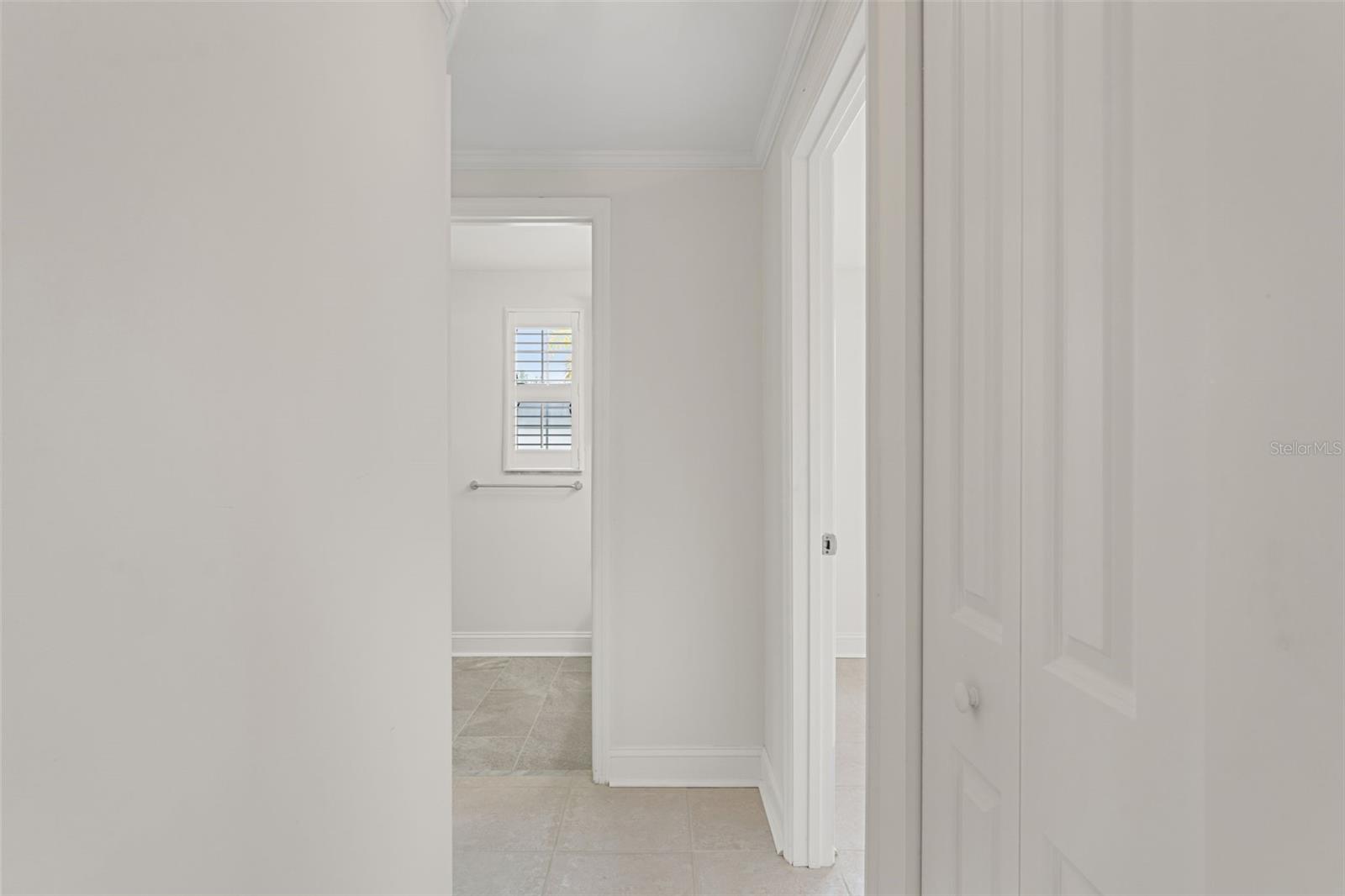 A fresh, neutral palette continues through the hallway leading to the private bedroom wing and updated bath, accented by plantation shutters for added style.