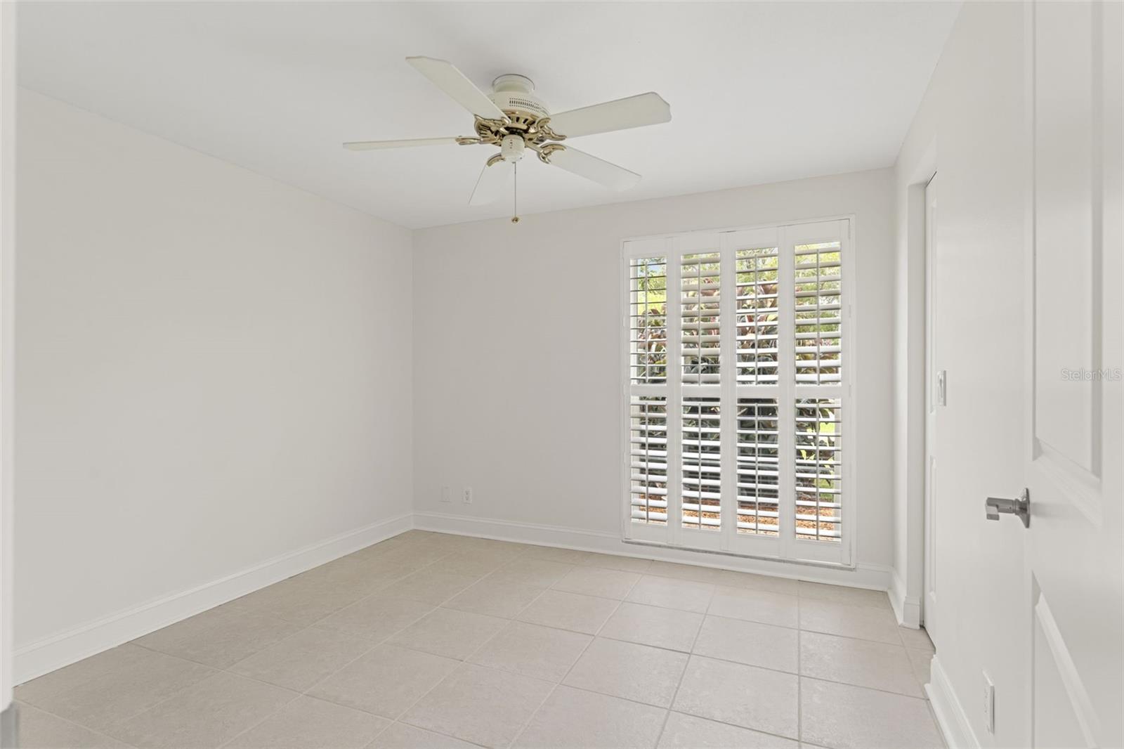 Peaceful retreat with plantation shutters, tile flooring, and a ceiling fan—creating a clean, airy feel.