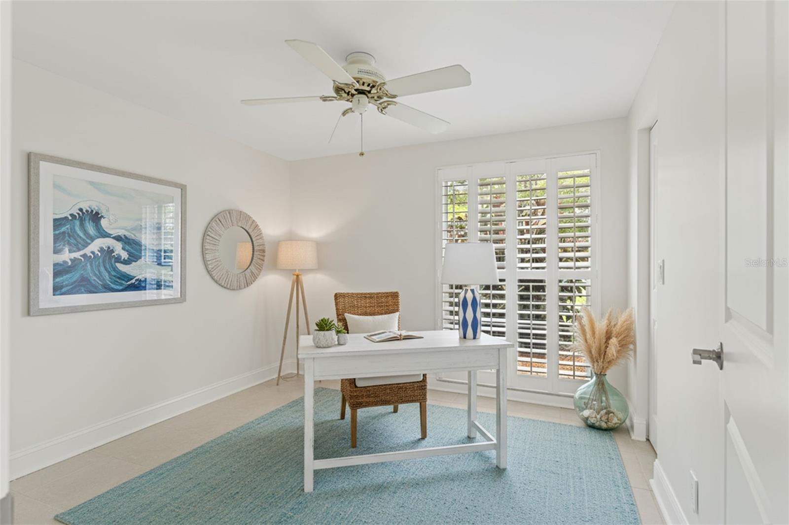 Light-filled room featuring plantation shutters, neutral tile flooring, and a serene coastal palette—ideal for a home office, guest room, or creative studio.