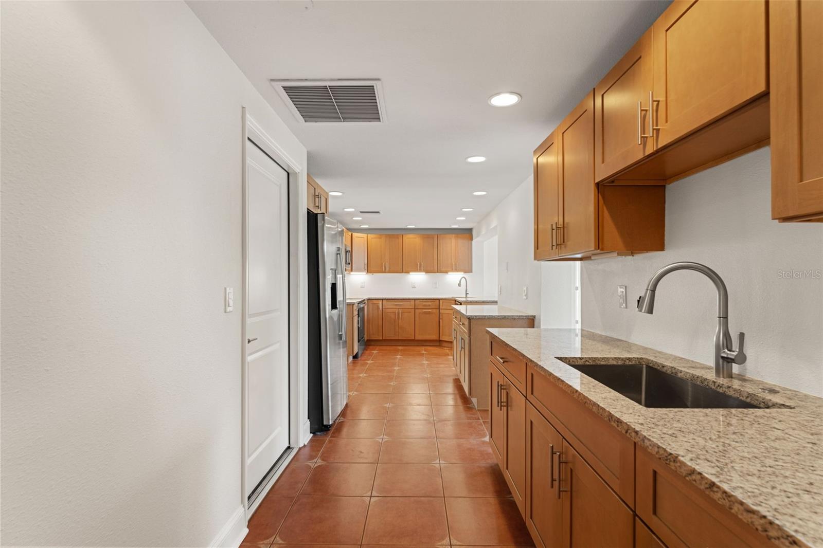 Thoughtfully designed layout connecting the laundry to the updated kitchen with wood cabinetry, granite counters, and stainless appliances.