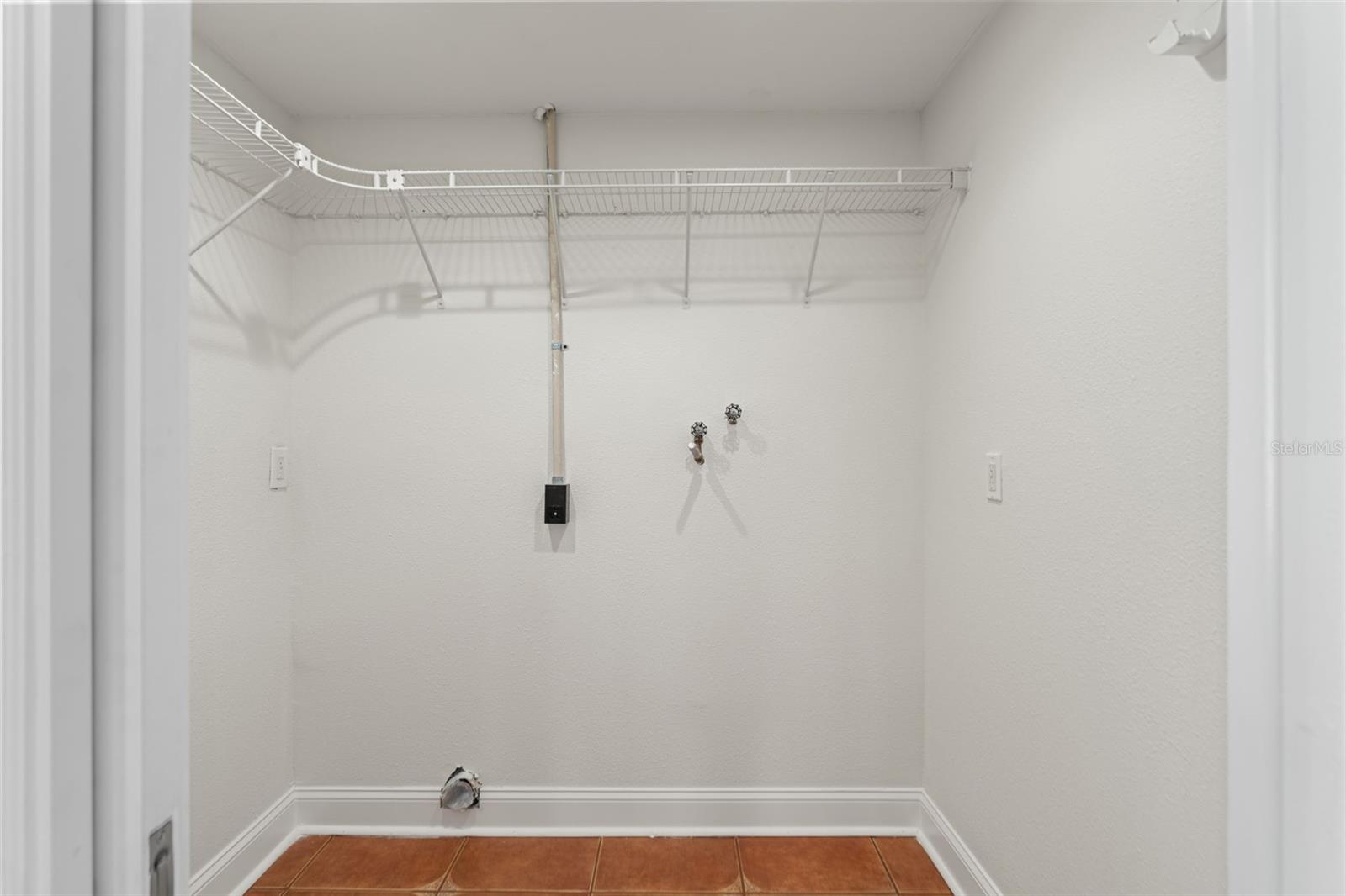 Convenient indoor laundry room with dedicated hookups, shelving, and extra space for storage or utility use.