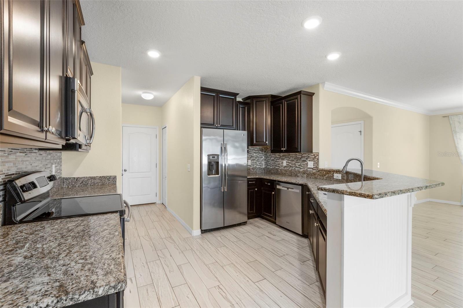Upgraded kitchen with granite counters, tile backsplash, multi-level solid wood cabinets, stainless steel appliances, breakfast bar with wainscoting details, pantry