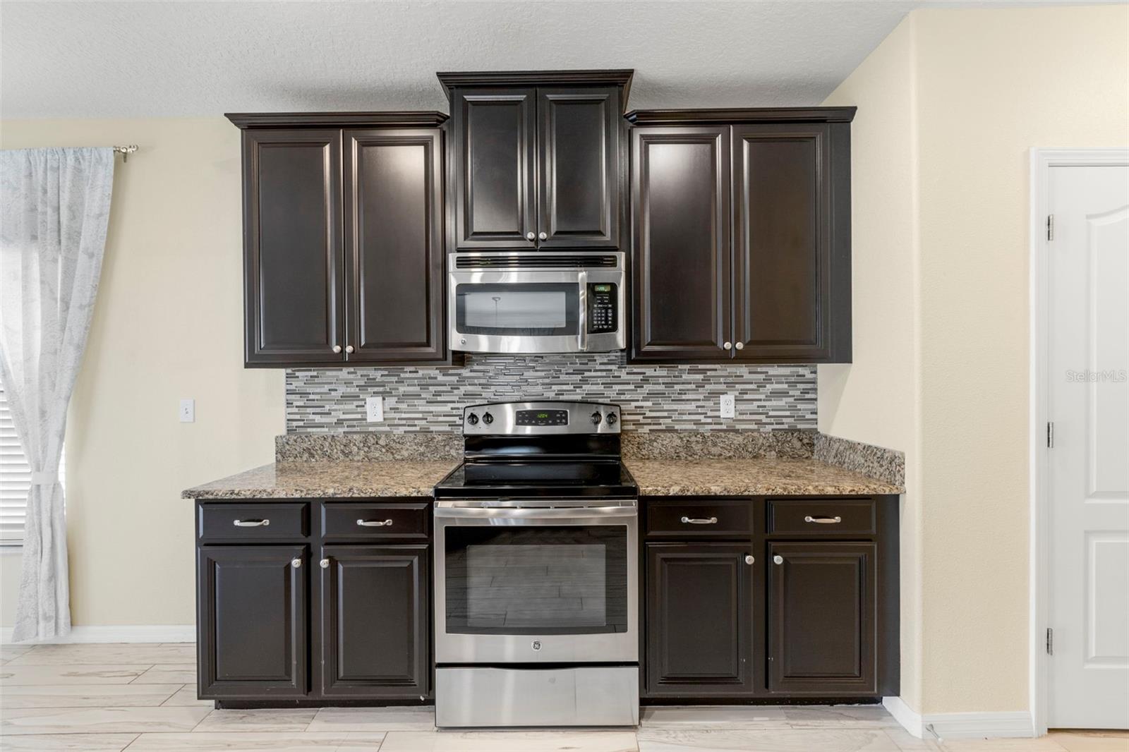 Upgraded kitchen with granite counters, tile backsplash, multi-level solid wood cabinets, stainless steel appliances, breakfast bar with wainscoting details, pantry