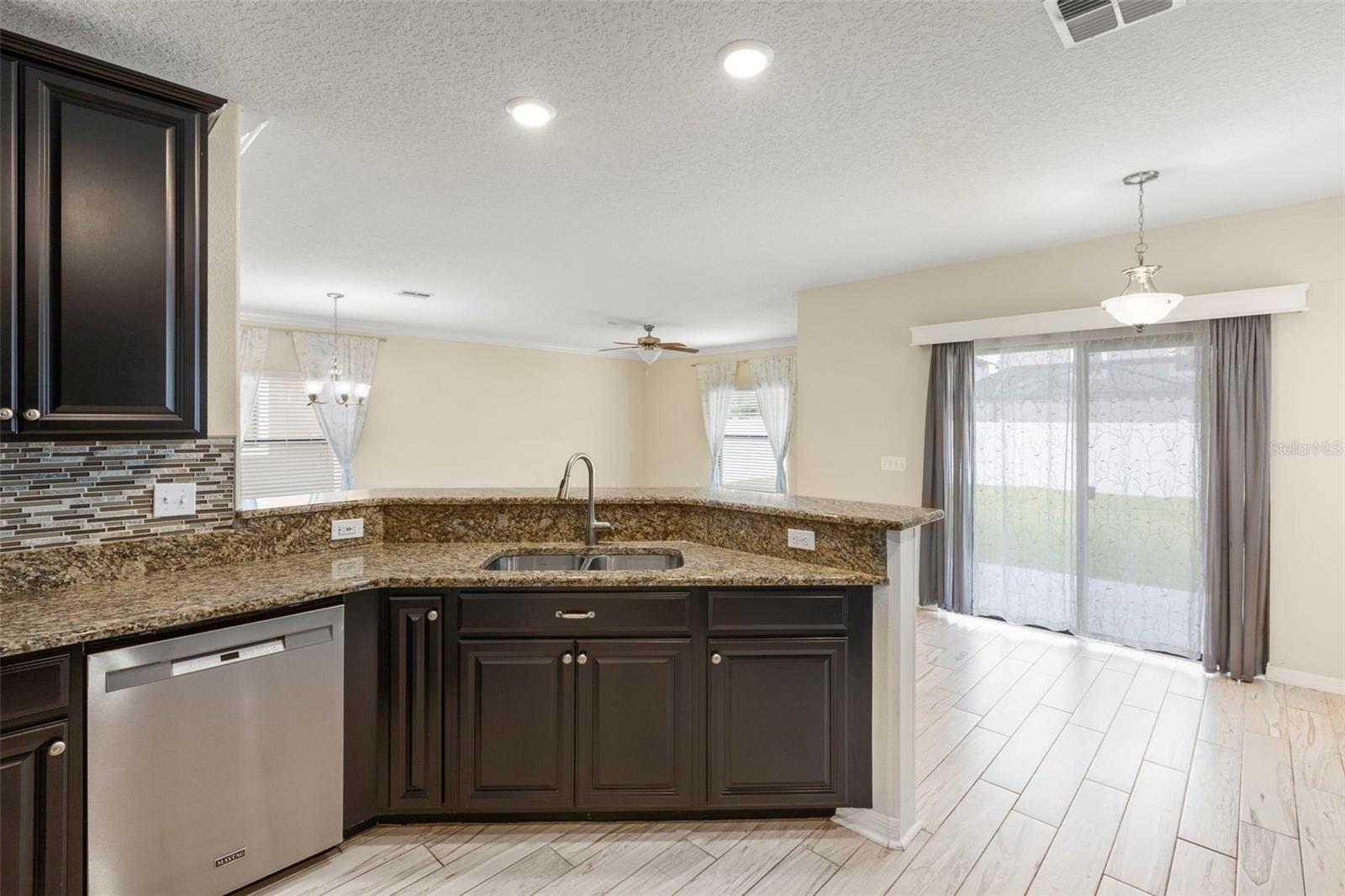 Upgraded kitchen with granite counters, tile backsplash, multi-level solid wood cabinets, stainless steel appliances, breakfast bar with wainscoting details, pantry