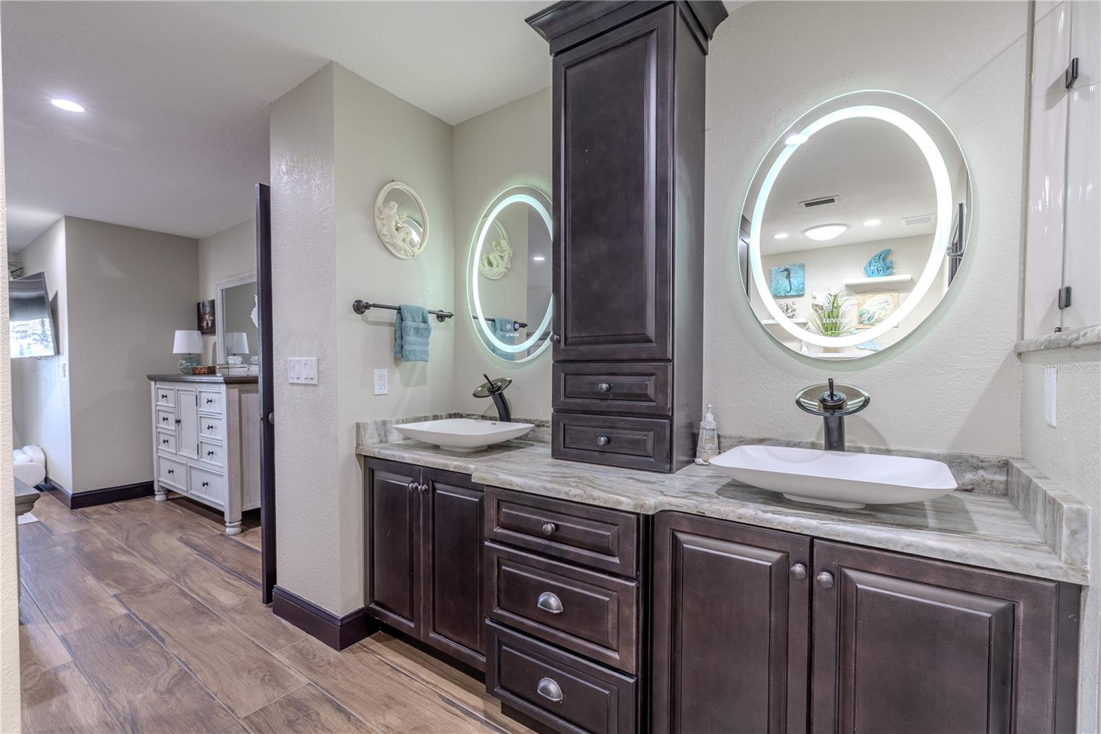 The primary bath showcases stunning split vanities with stone countertops, LED lighted mirrors, and custom water faucets chosen for their sleek and artistic design.