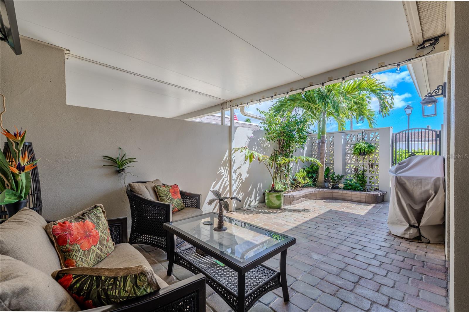 The front patio courtyard offers a peaceful outdoor retreat with brick pavers, a mounted fan, and direct access to both the garage and the second bedroom.