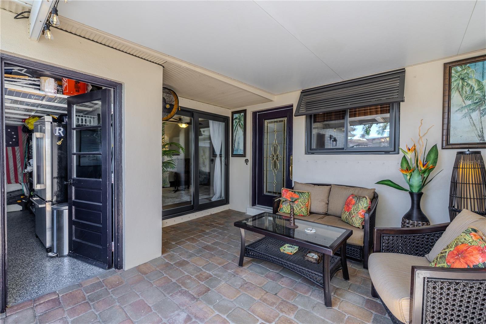 The front patio courtyard offers a peaceful outdoor retreat with brick pavers, a mounted fan, and direct access to both the garage and the second bedroom.