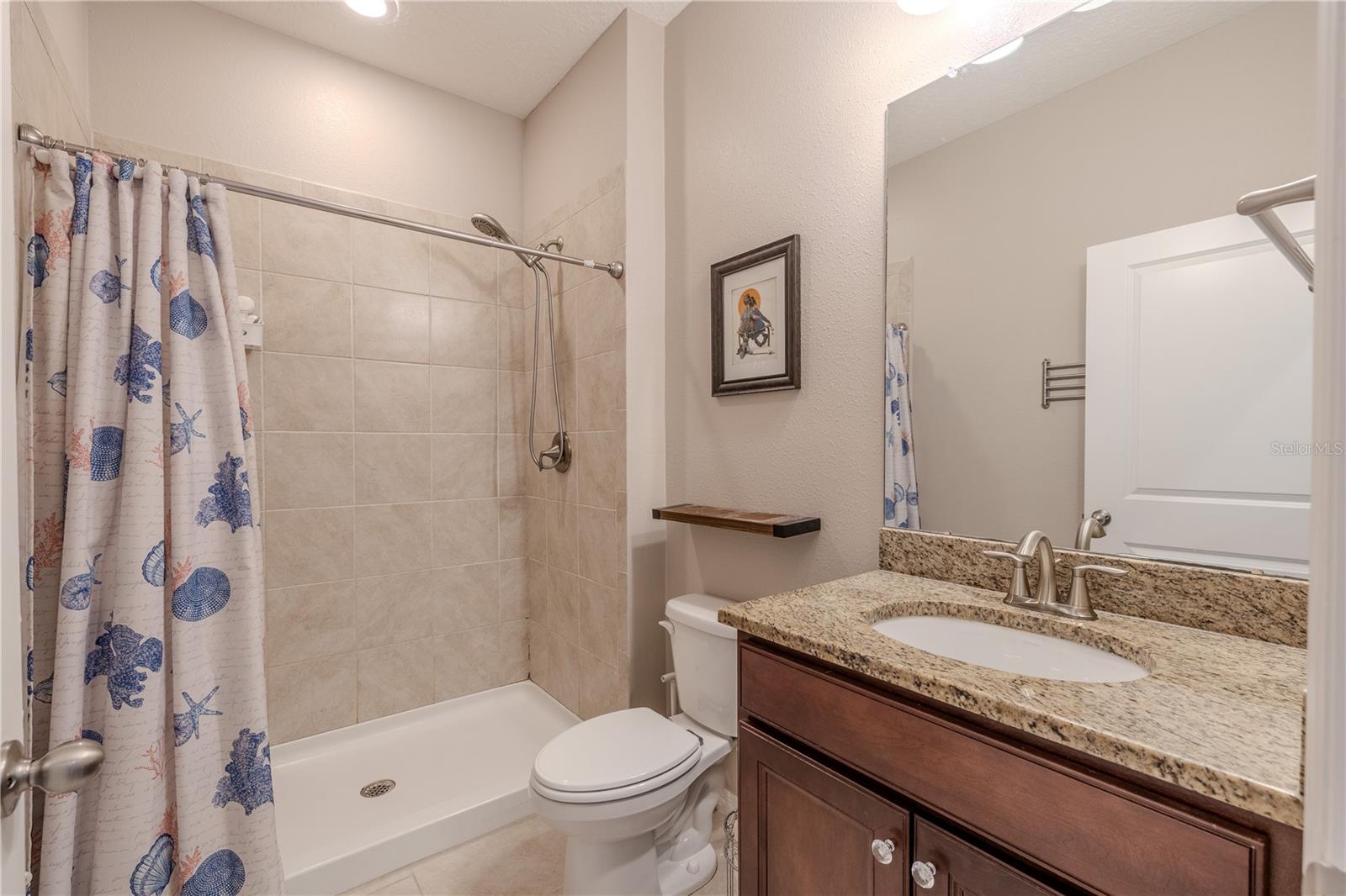 Full first-floor guest bath featuring granite vanity, modern fixtures, and a tile shower for easy accessibility.