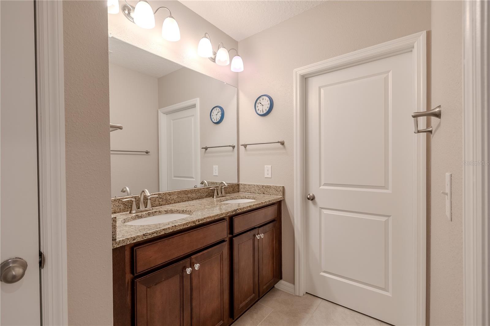 Additional view of the upstairs bath highlighting the extended vanity, upgraded fixtures, and warm wood cabinetry.