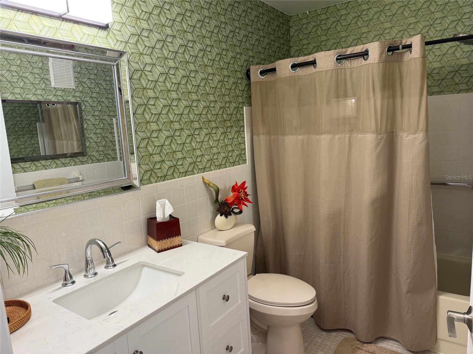 Guest bath is steps away from guest bedroom.  This updated bathroom features a tub with shower, new vanity and comfort height commode.
