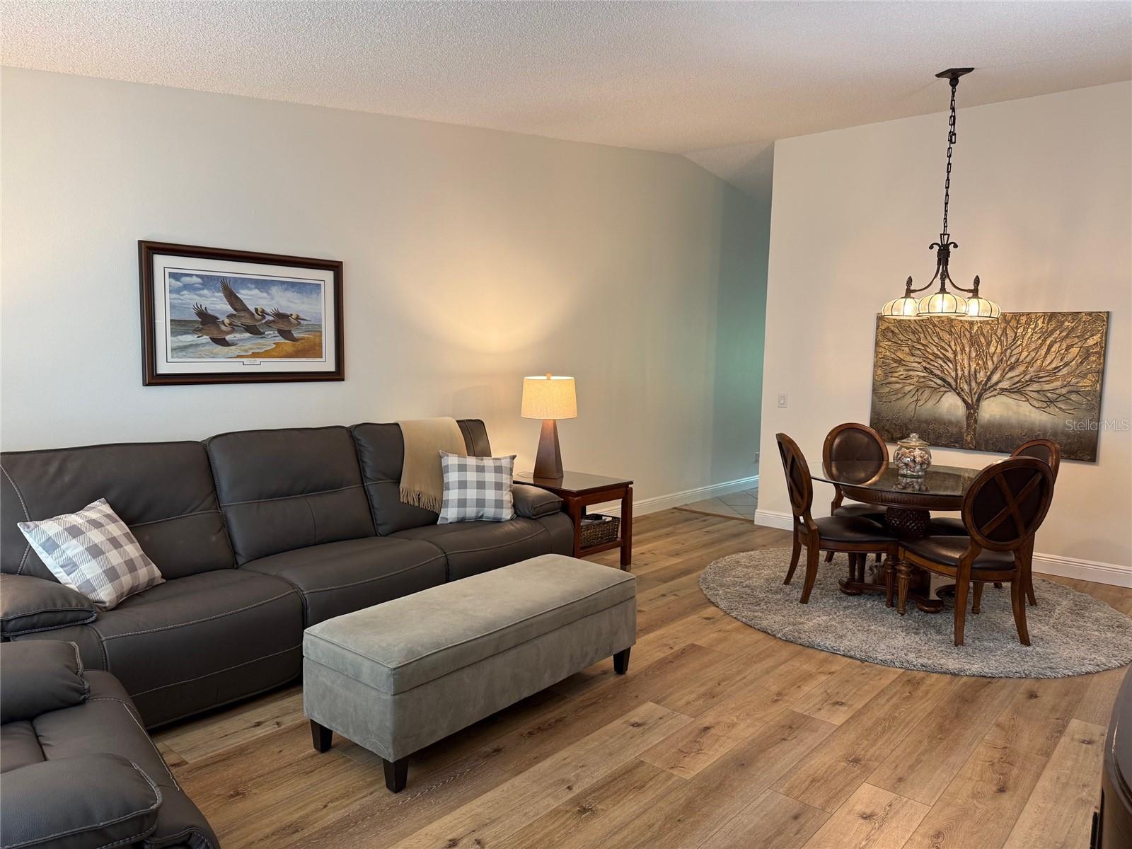 View of hallway leading to kitchen/Florida room area.  Both bedrooms & baths are to the right.  Interior features recently painted, neutral decor (2024) and updated luxary vinyl flooring.  New hanging light over dining room table.