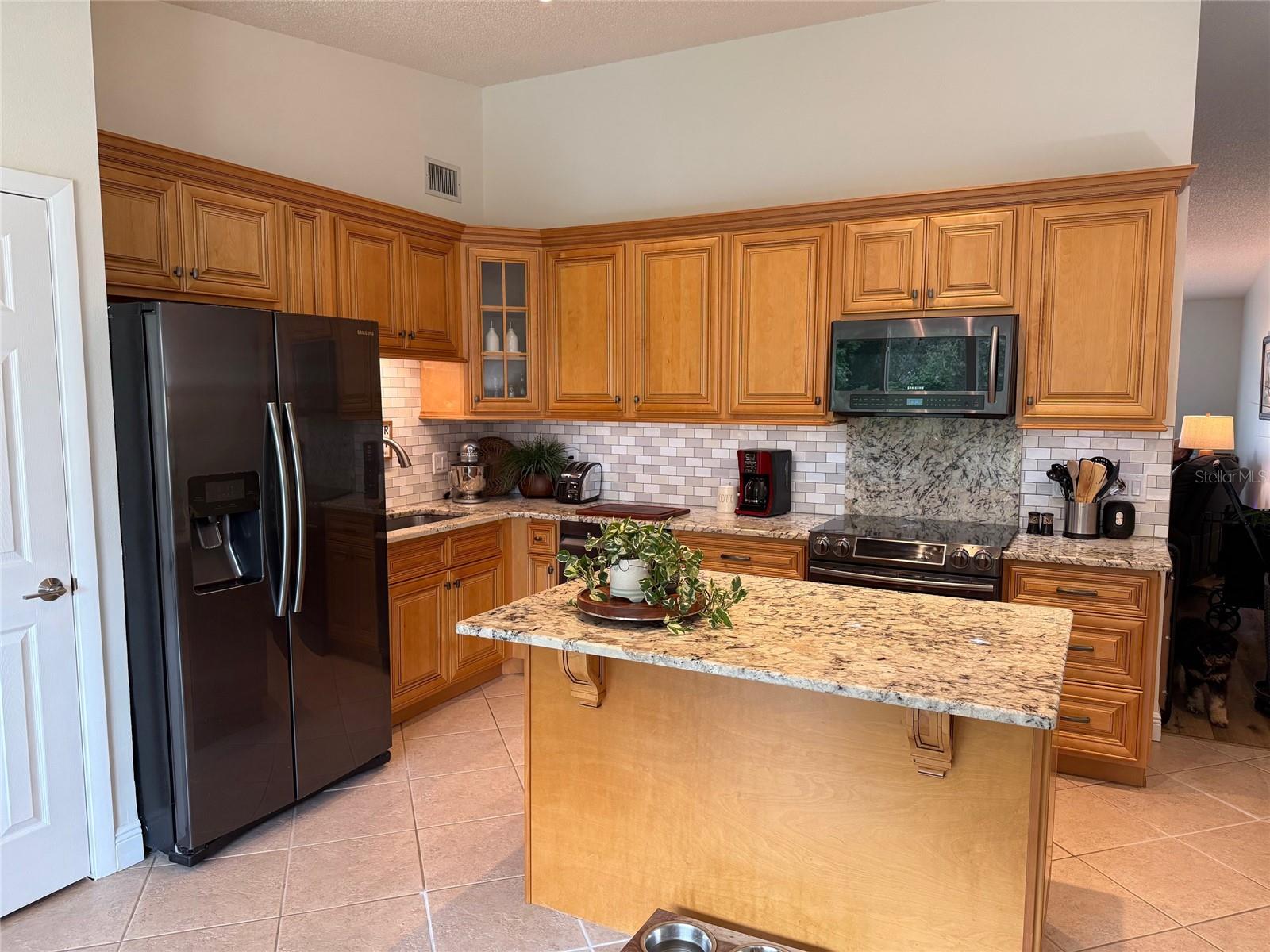 View from Florida room of Kitchen to hallway into living/dining room.  This stunning kitchen features "Exotic" granite countertops, glass tile backsplash, black stainless Samsung appliances and Maple wood cabinetry.  Pantry is to the left.  Awesome kitchen island anchors the kitchen.