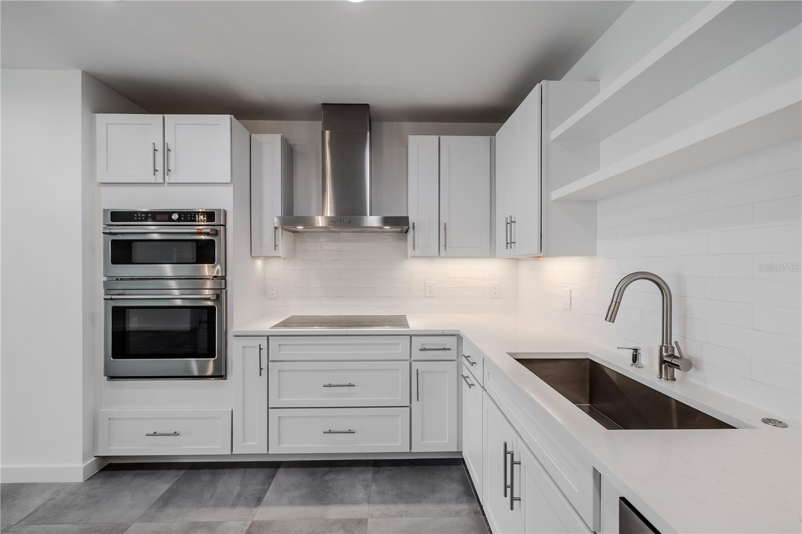 High-end stainless-steel appliances include a French door refrigerator, dishwasher, double wall ovens, and a vent hood. Large  tile floors and under-cabinet lighting complete this bright, sophisticated culinary space.