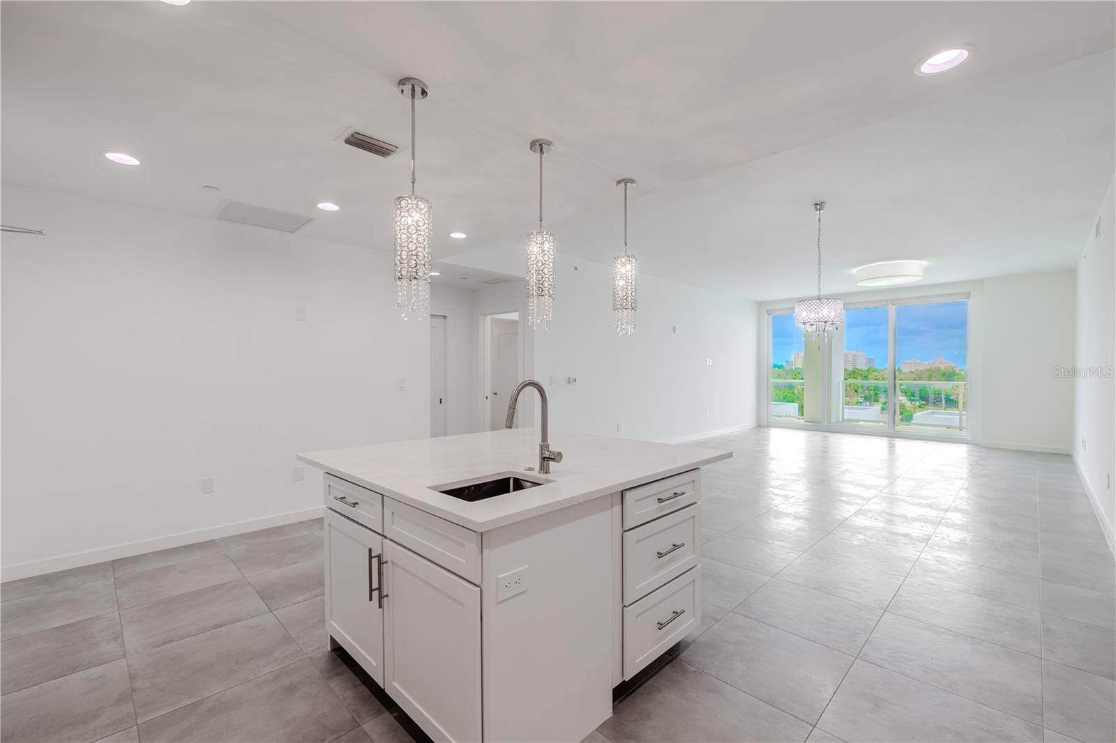 From the kitchen, enjoy an open-concept view that seamlessly connects the dining and living areas. Sleek tile flooring and designer lighting create a bright, contemporary flow, while floor-to-ceiling sliding glass doors frame lush treetop and skyline views beyond the spacious balcony