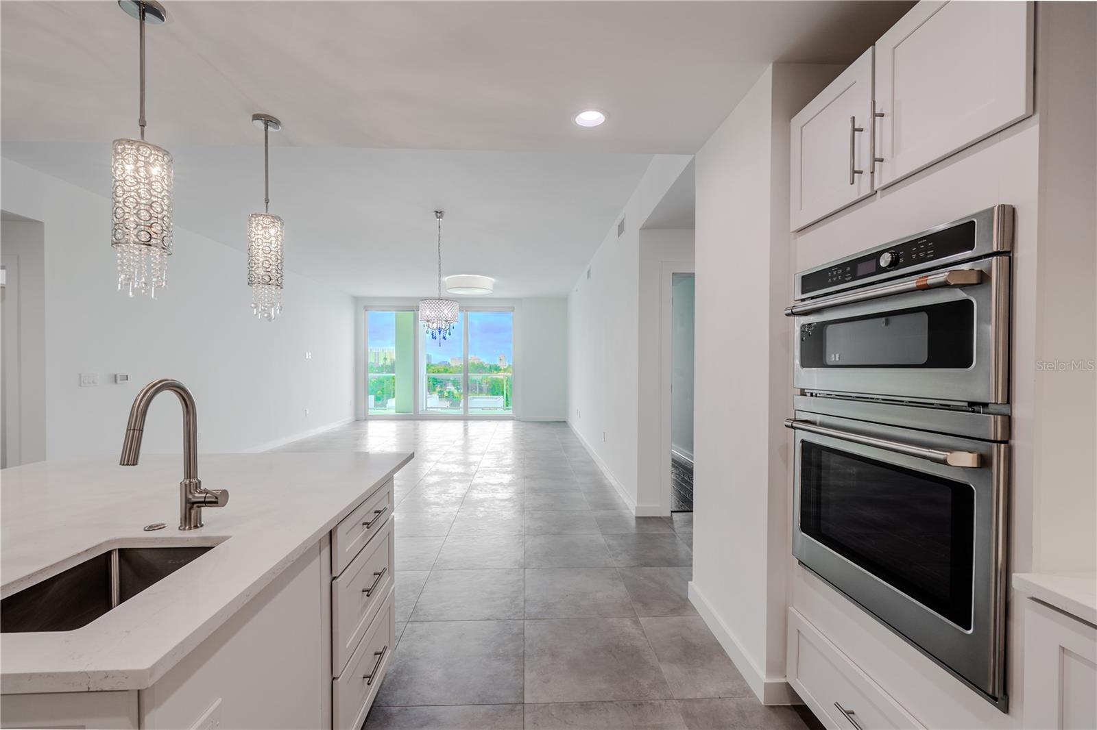 From the kitchen, enjoy an open-concept view that seamlessly connects the dining and living areas. Sleek tile flooring and designer lighting create a bright, contemporary flow, while floor-to-ceiling sliding glass doors frame lush treetop and skyline views beyond the spacious balcony