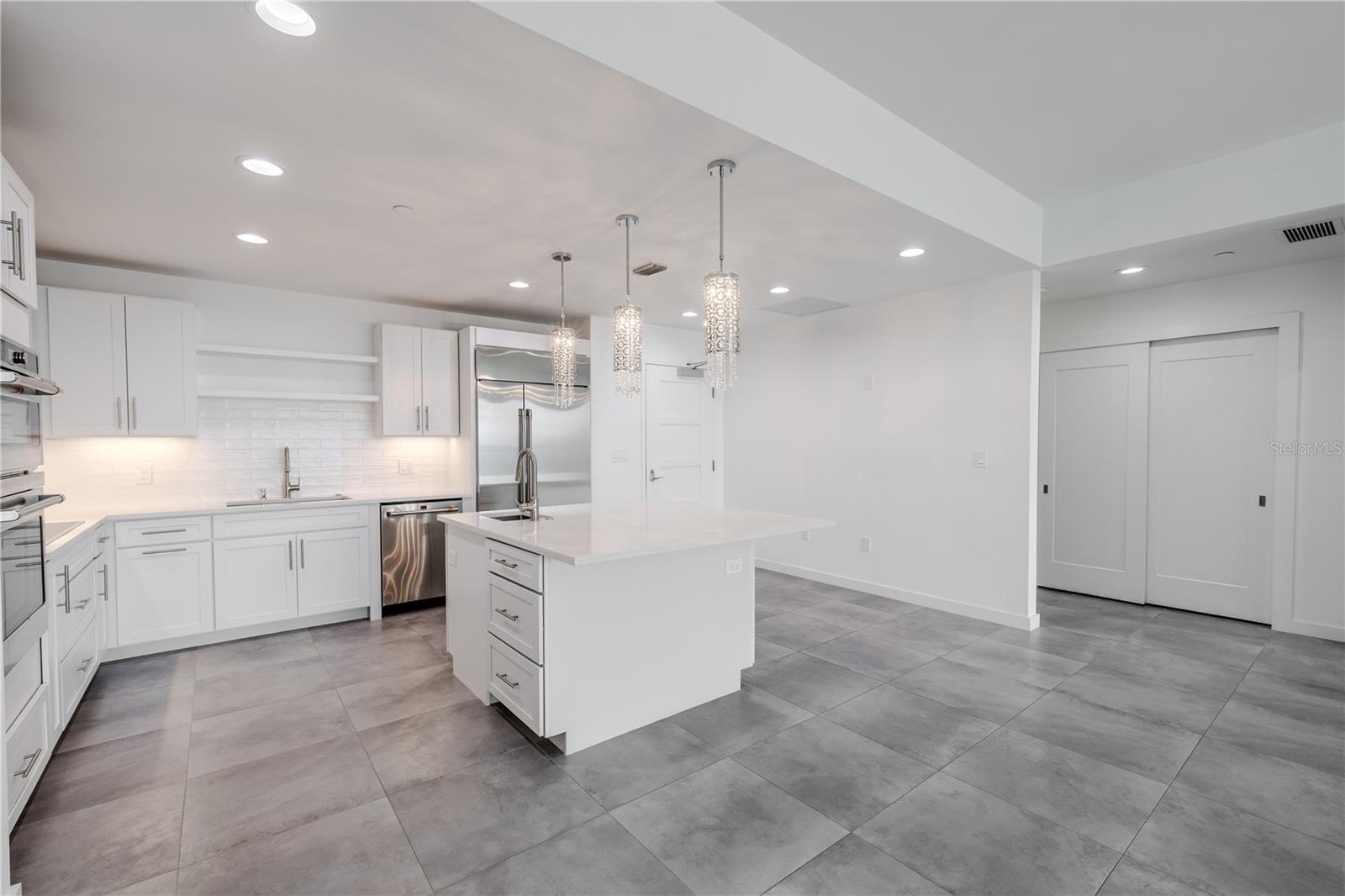 High-end stainless-steel appliances include a French door refrigerator, dishwasher, double wall ovens, and a vent hood. Large  tile floors and under-cabinet lighting complete this bright, sophisticated culinary space.