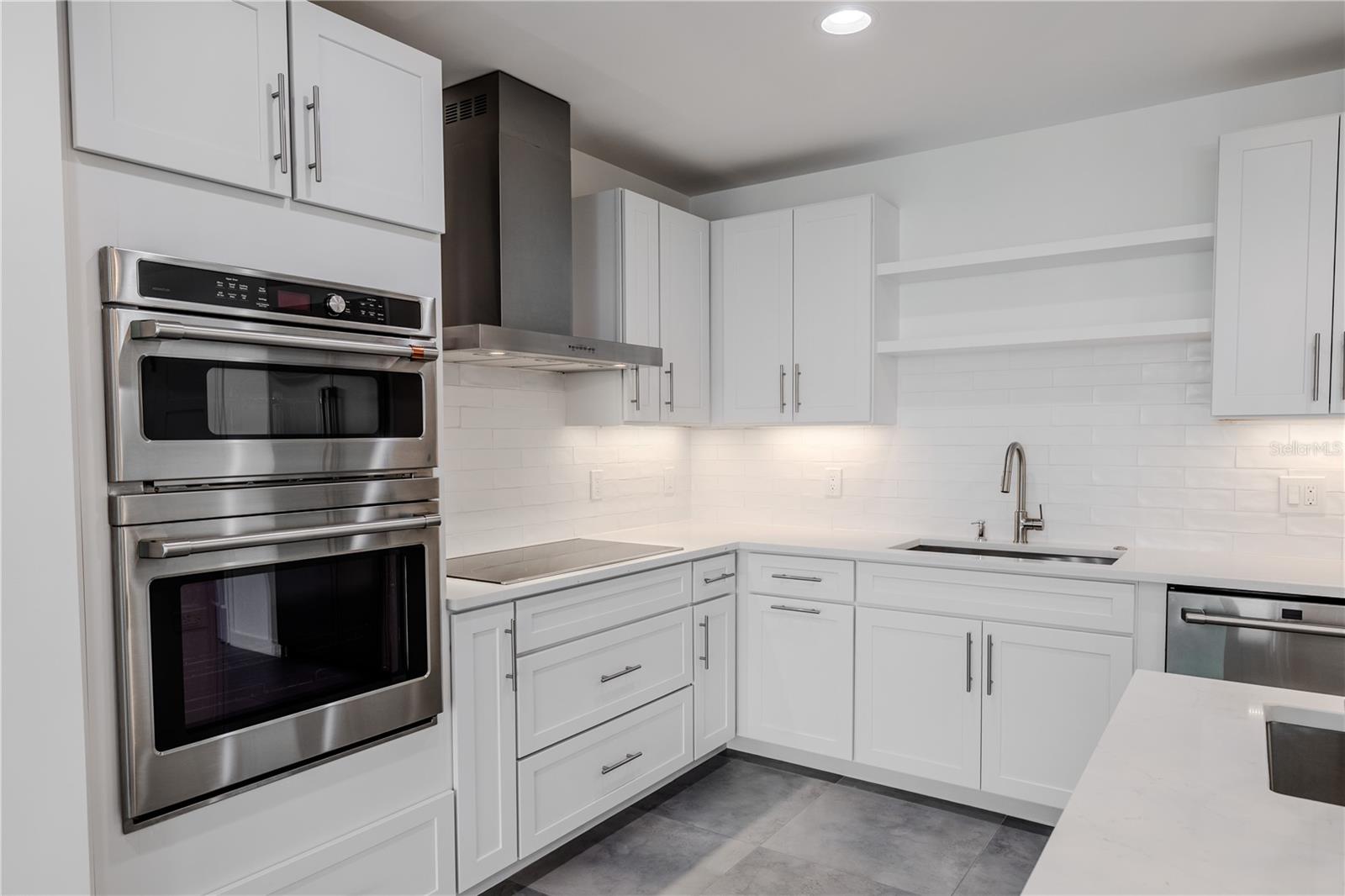 Under-cabinet lighting enhances the glossy subway tile backsplash, while open shelving adds a contemporary touch. Every detail reflects quality, functionality, and timeless style.