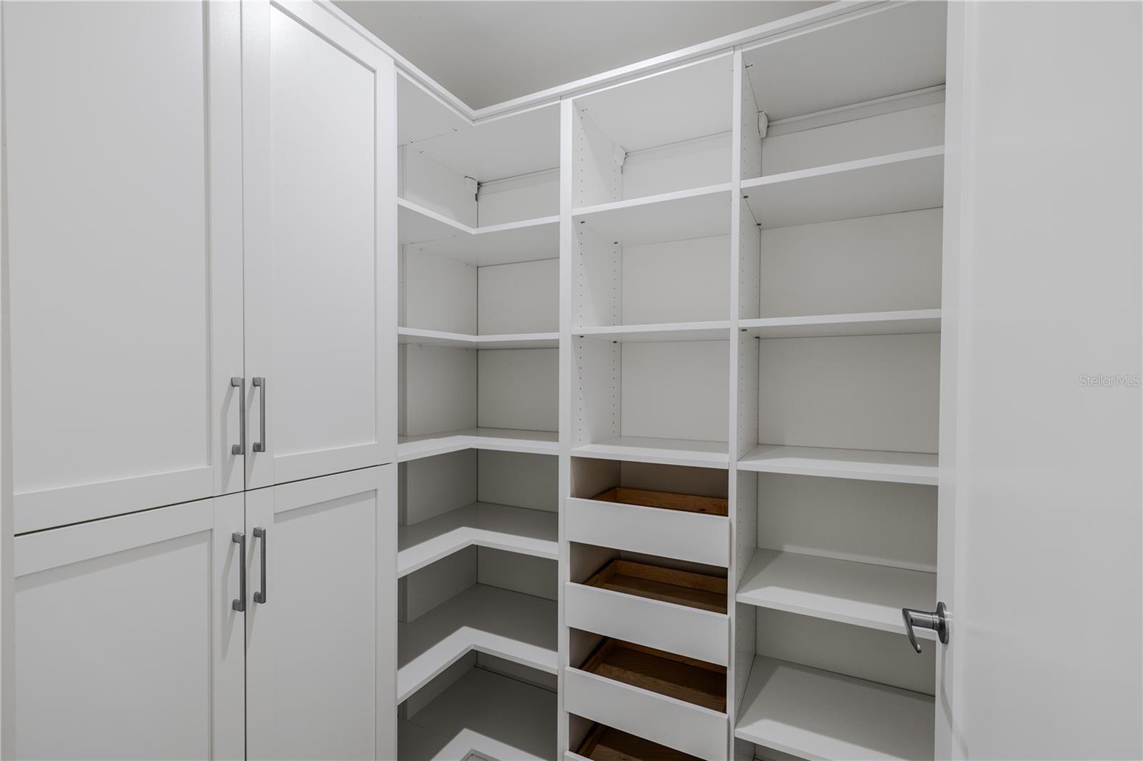 Spacious walk-in pantry with custom built-in shelving, ample storage, and pull-out drawers for easy organization. Clean white cabinetry and adjustable shelves provide both functionality and a polished, modern look.