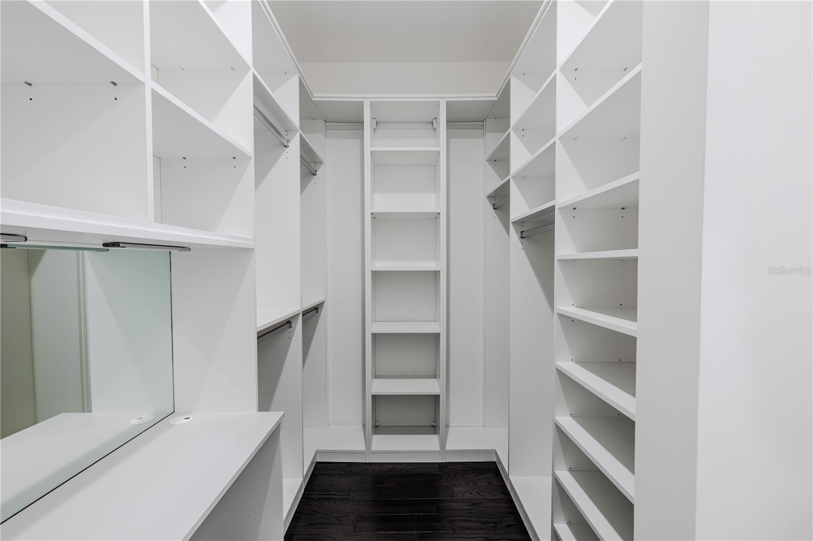 The first primary walk-in closet offers abundant storage with custom built-in shelving, double hanging rods, and open cubbies designed for effortless organization. Clean lines and bright white finishes create a polished, boutique-style space, perfect for keeping wardrobe essentials neatly displayed and within easy reach. Ideal for those who appreciate both form and function.
