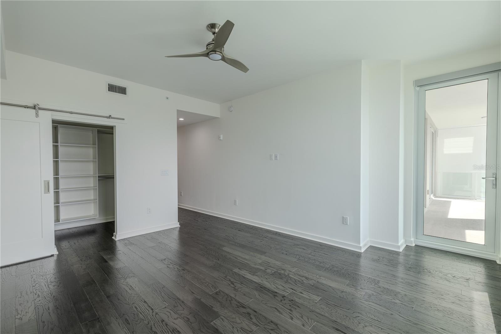 Bedroom 2 features sleek hardwood flooring, a modern ceiling fan, and direct access to the balcony, allowing natural light to flow throughout the room. A custom-built closet with sliding barn-style doors provides efficient storage and a touch of contemporary design.