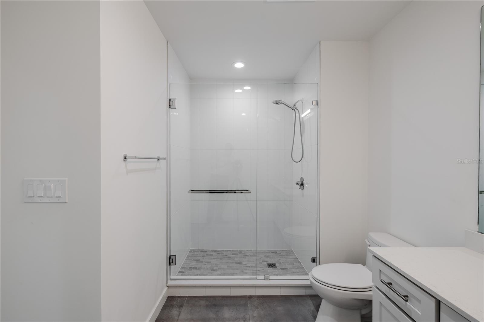 The ensuite bath for Bedroom 3 is beautifully appointed with clean modern lines and high-end finishes. A frameless glass walk-in shower with polished chrome fixtures and a handheld sprayer anchors the space, complemented by large-format tile flooring and crisp white wall tile for a bright, spa-like atmosphere.
