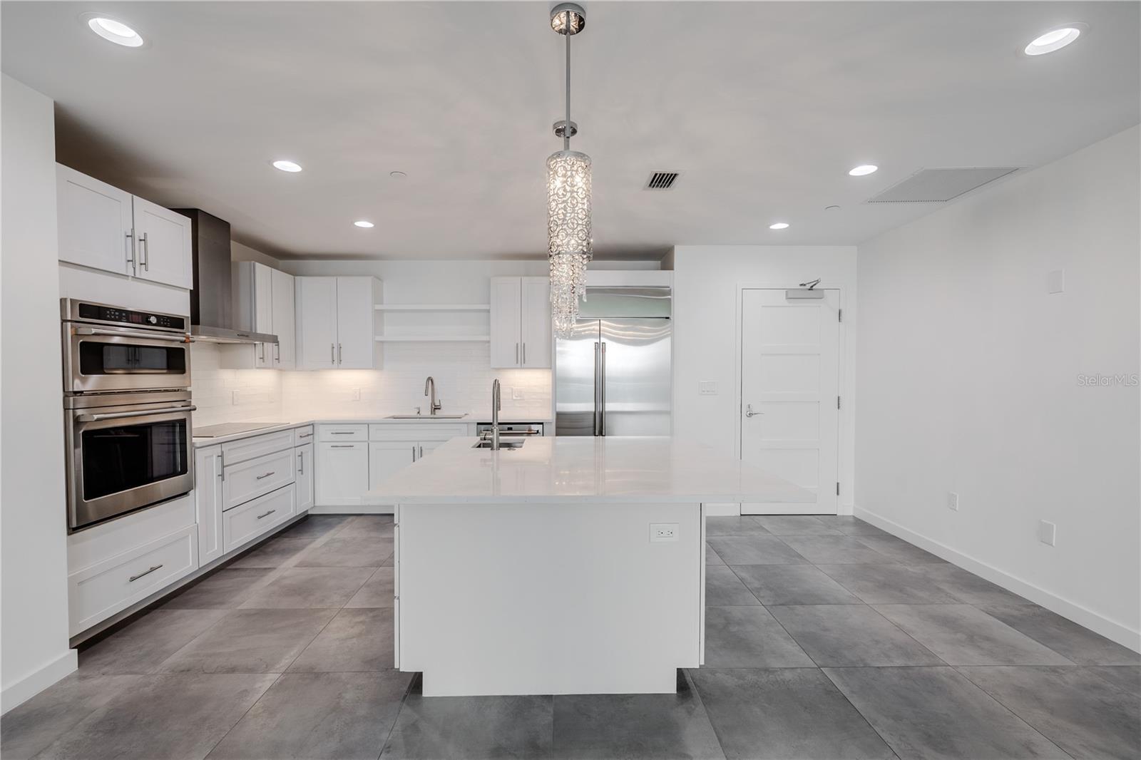 The kitchen features sleek white solid-wood cabinetry, soft-close drawers, and a full suite of stainless-steel appliances including a French door refrigerator, double wall ovens, and a range hood.