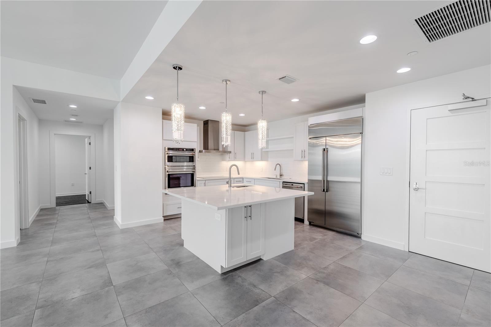 This show stopping modern kitchen is the centerpiece of the home, designed for both style and functionality. A sleek quartz island with storage and sink and bar seating anchors the open concept layout, framed by elegant crystal pendant lighting that adds a touch of glamour.