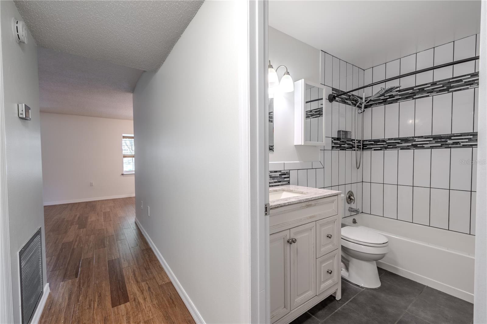 The bathroom features a stylish, modern design with clean lines and finishes. The tub-shower combo is accented by striking vertical white tile with a contrasting horizontal mosaic band for a touch of contemporary flair.