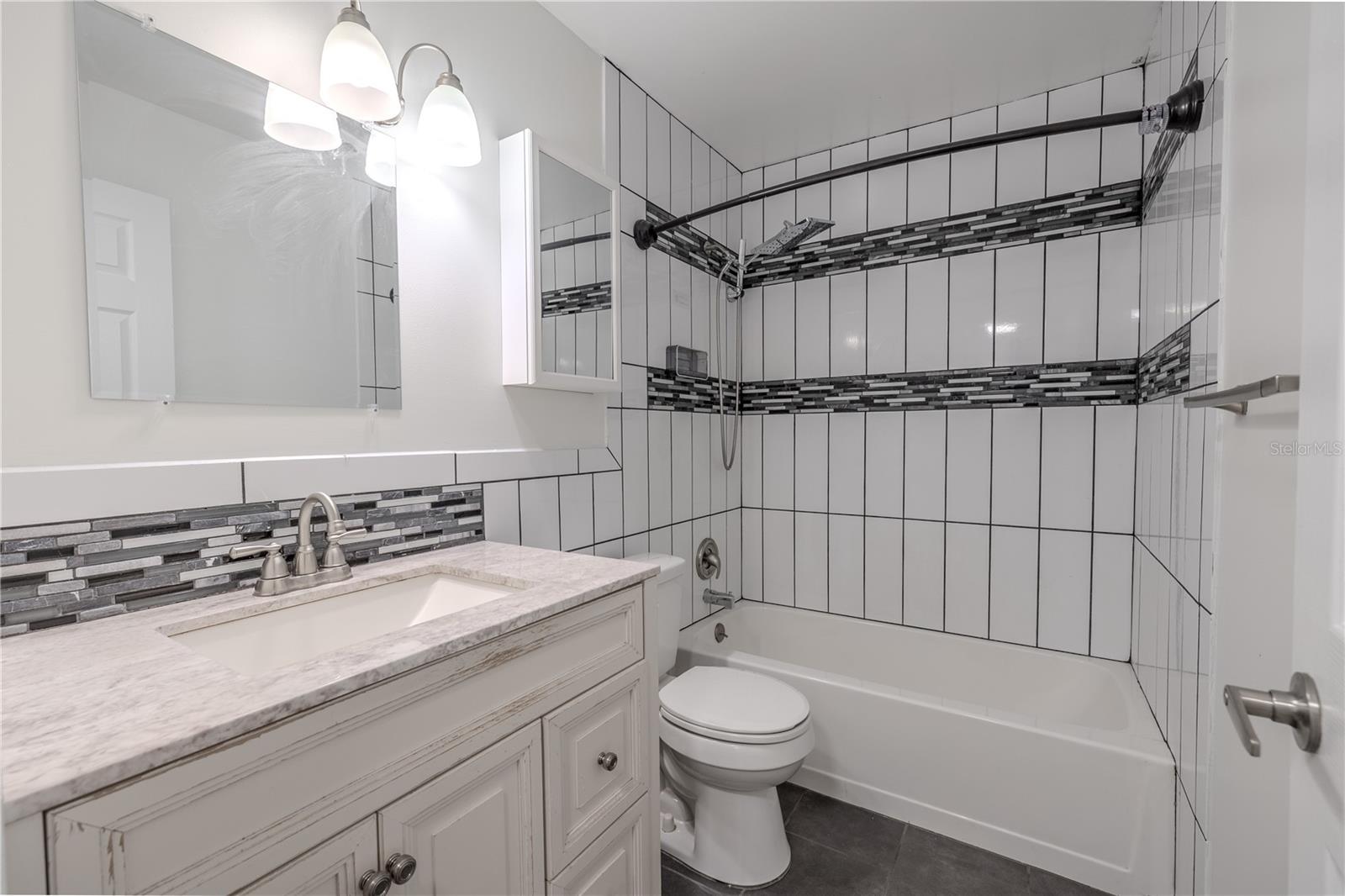 A classic vanity with a marble-look countertop provides both charm and functionality, complemented by brushed nickel fixtures and updated lighting.