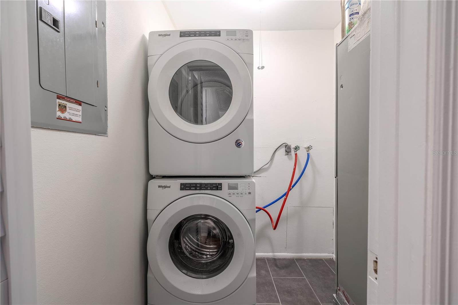 The laundry room offers a convenient and efficient setup with a modern Whirlpool washer and dryer stacked to maximize space. The area is well-lit and features easy-to-access water connections and tile flooring for durability and easy maintenance. Its practical layout provides functionality without sacrificing style, making laundry tasks simple and organized.