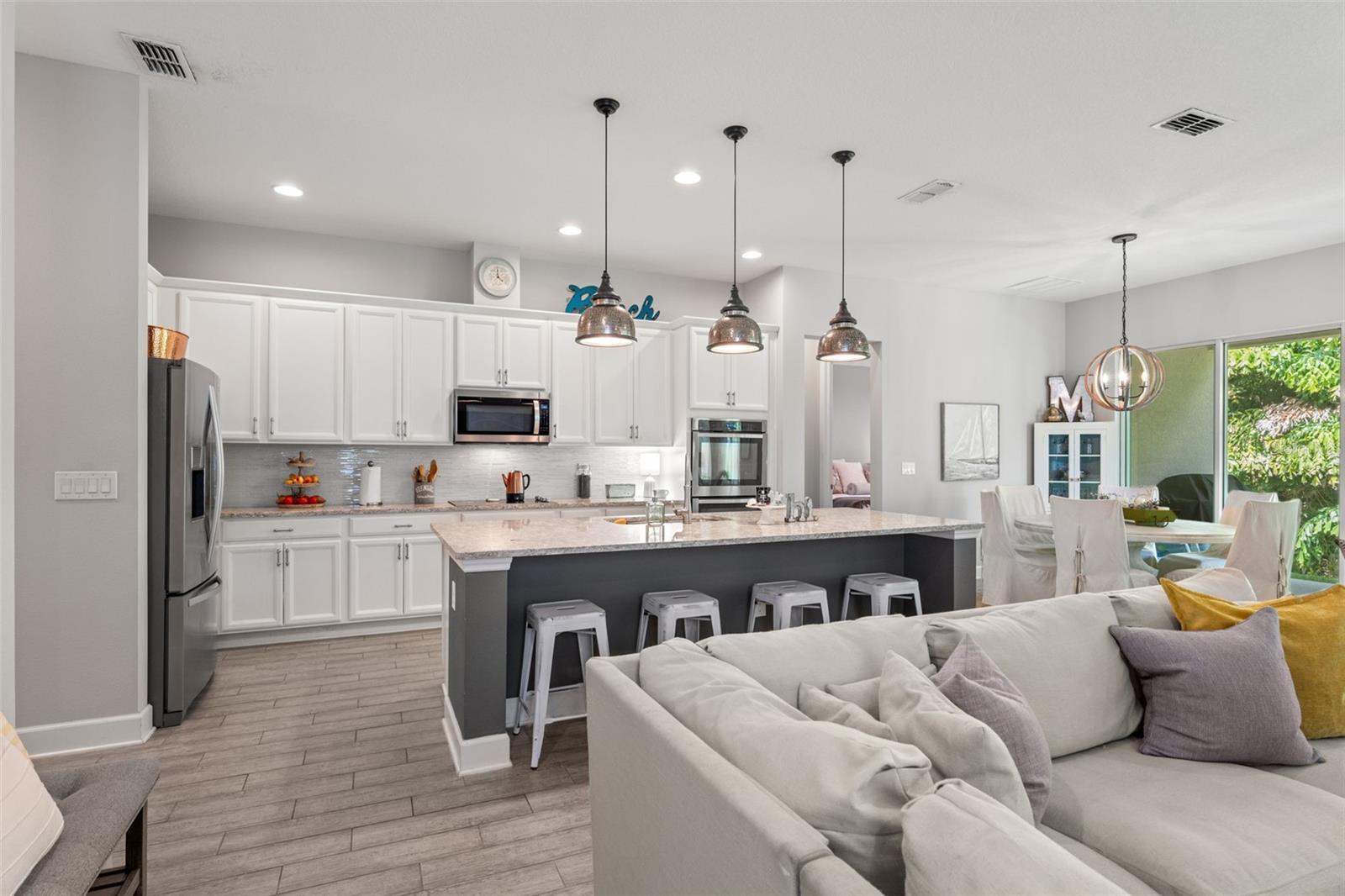 Bright and beautifully appointed kitchen with white shaker cabinets, granite countertops, stainless steel appliances, and a large center island with breakfast bar seating.