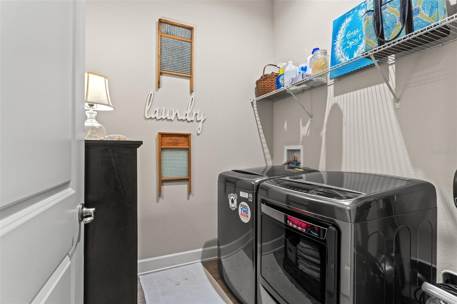 Well-organized laundry room featuring high-efficiency washer and dryer, decorative shelving, and space for additional storage.