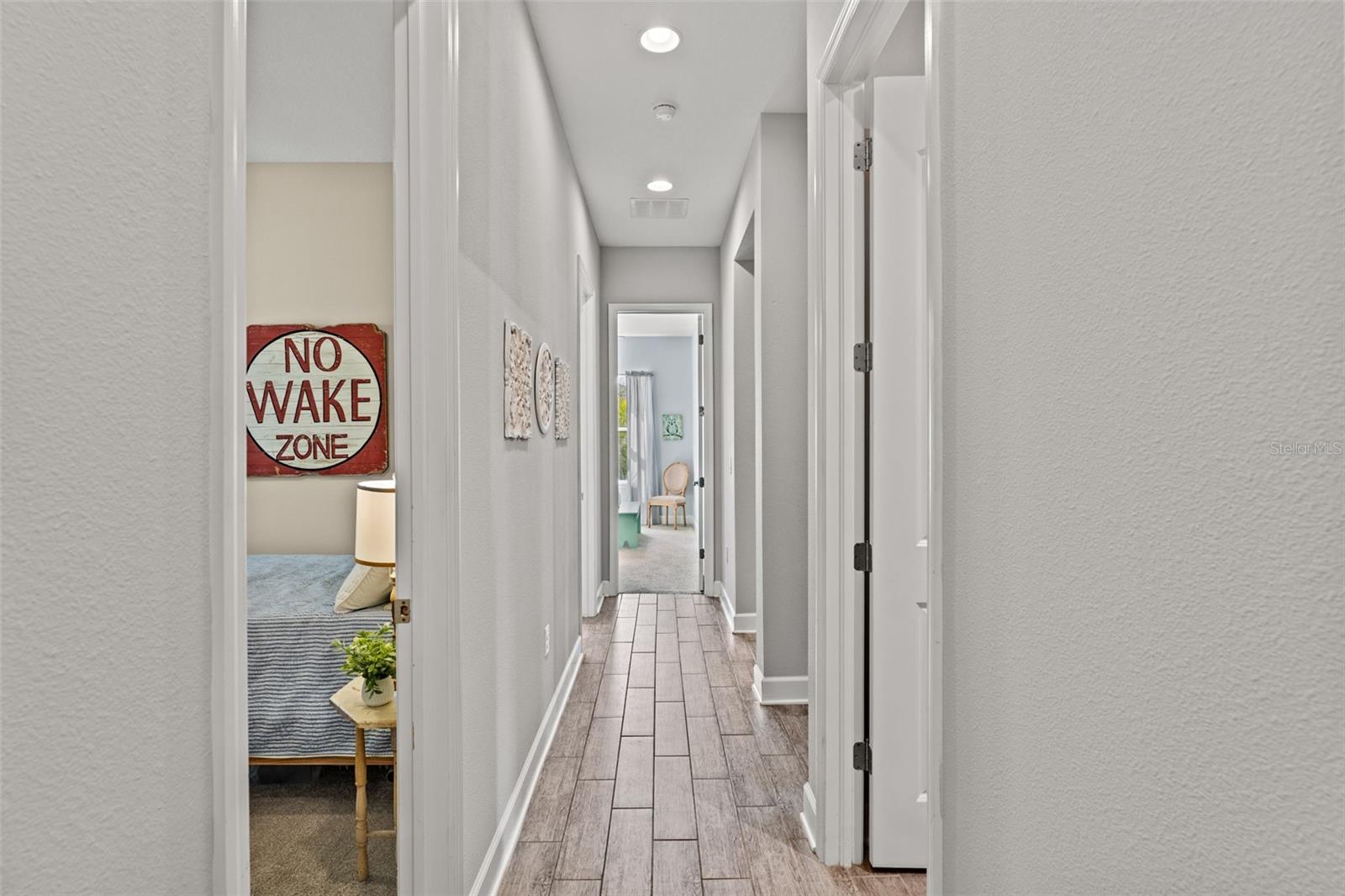 Wide hallway connecting the additional bedrooms and bath, accented by modern tile flooring and soft recessed lighting.